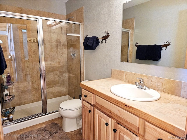 bathroom with a textured wall, a shower stall, toilet, and vanity