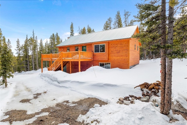 snow covered house featuring stairs, metal roof, and a wooden deck