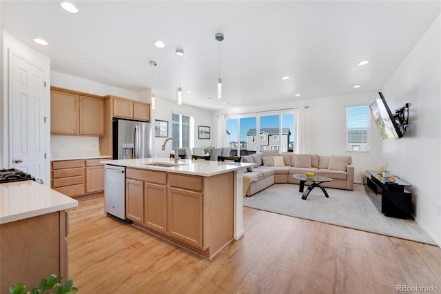 kitchen with decorative light fixtures, sink, stainless steel appliances, a center island with sink, and light wood-type flooring