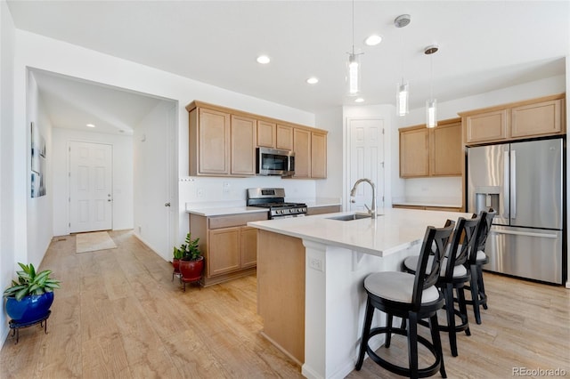 kitchen with sink, light hardwood / wood-style flooring, appliances with stainless steel finishes, an island with sink, and pendant lighting