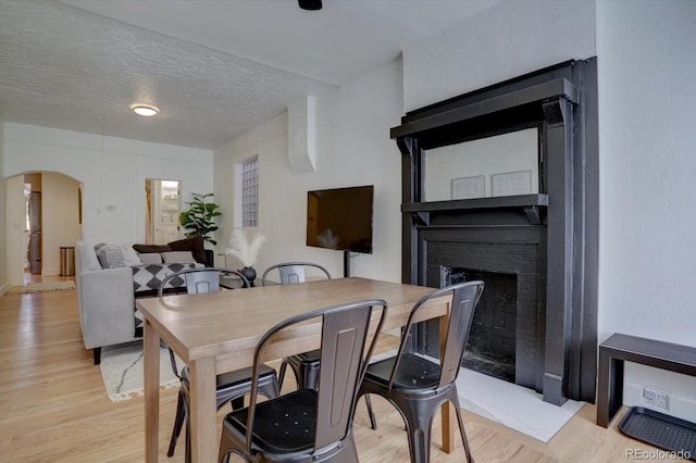 dining room with arched walkways, a textured ceiling, a brick fireplace, and light wood finished floors