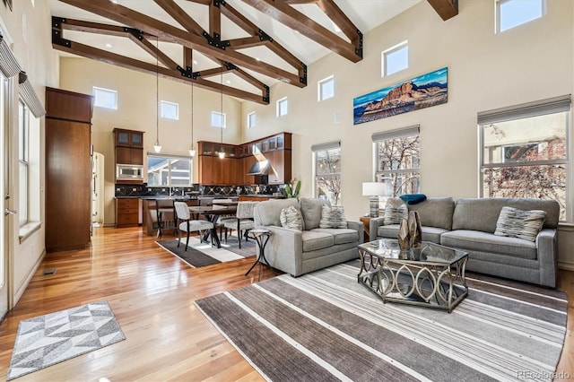 living area featuring lofted ceiling with beams, light wood-style flooring, and visible vents