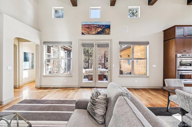 living room with arched walkways, wood finished floors, a towering ceiling, baseboards, and beamed ceiling