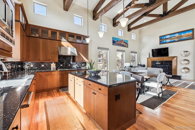 kitchen featuring pendant lighting, glass insert cabinets, open floor plan, a sink, and under cabinet range hood