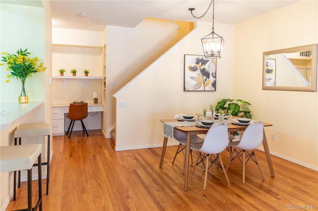 dining room with light wood-type flooring, an inviting chandelier, and built in desk