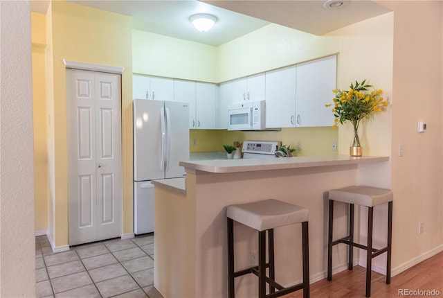 kitchen featuring a kitchen breakfast bar, white appliances, and white cabinets