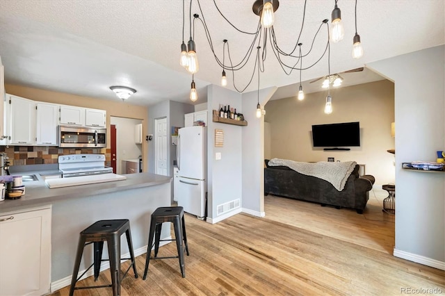 11376 Forest Dr, Thornton, CO 80233 - kitchen with white appliances, light wood-style floors, white cabinetry, tasteful backsplash, and a peninsula