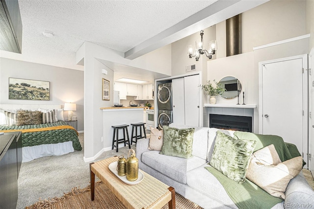 carpeted living room featuring a textured ceiling, a tile fireplace, a notable chandelier, a high ceiling, and stacked washer / drying machine