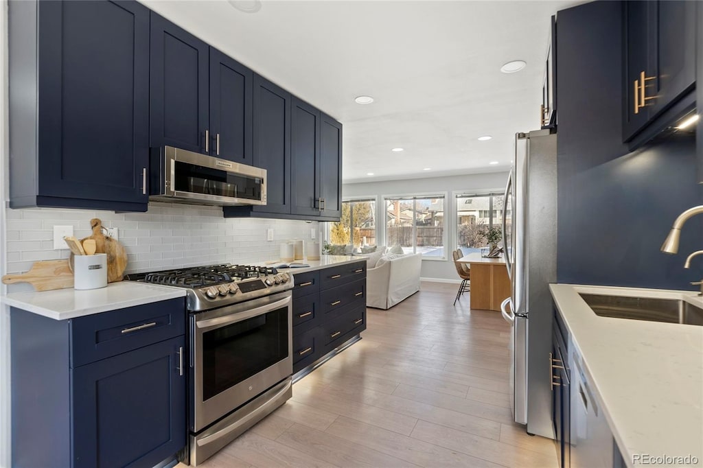 kitchen with stainless steel appliances, light wood-type flooring, blue cabinetry, light stone counters, and sink