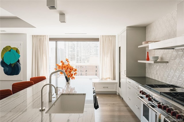 kitchen featuring sink, range with two ovens, wall chimney range hood, and a healthy amount of sunlight