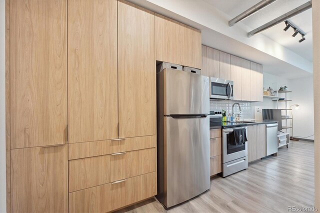 kitchen featuring appliances with stainless steel finishes, sink, light wood-type flooring, backsplash, and light brown cabinets