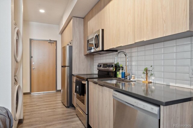 kitchen featuring appliances with stainless steel finishes, light brown cabinets, stacked washer and dryer, and light hardwood / wood-style floors