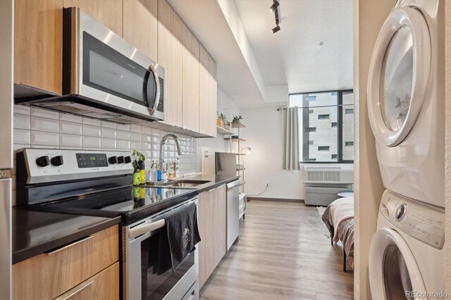 kitchen with decorative backsplash, stacked washer and dryer, stainless steel appliances, sink, and light wood-type flooring