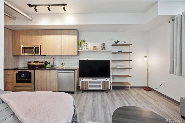 kitchen featuring light brown cabinetry, sink, light hardwood / wood-style floors, stainless steel appliances, and decorative backsplash