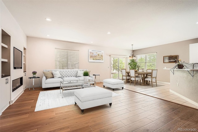 living area featuring wood finished floors, recessed lighting, a glass covered fireplace, and baseboards