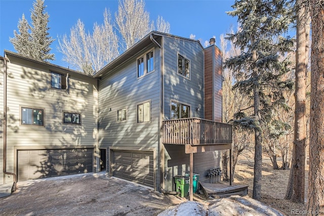 rear view of property with a garage, driveway, a chimney, and a balcony