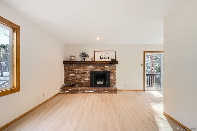 unfurnished living room with light wood-style floors, a brick fireplace, and baseboards