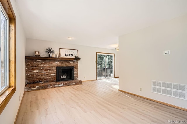 unfurnished living room featuring light wood-style floors, a brick fireplace, visible vents, and baseboards