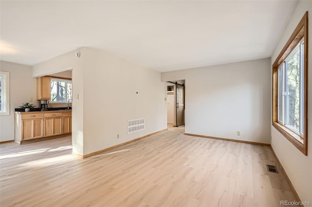 unfurnished room featuring light wood-style floors, visible vents, baseboards, and a barn door