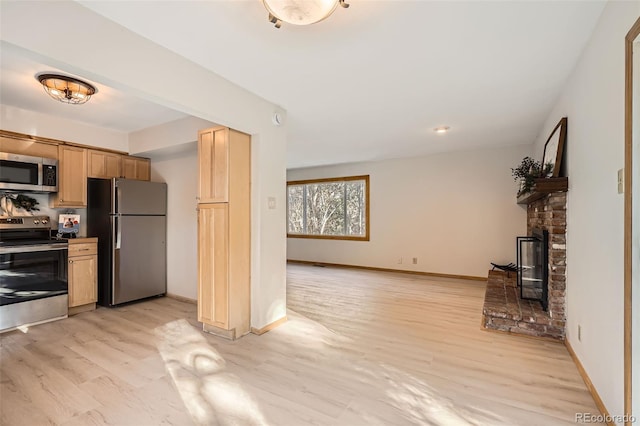 kitchen with a fireplace, baseboards, light wood-style floors, appliances with stainless steel finishes, and light brown cabinetry