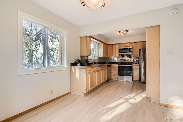 kitchen featuring light wood finished floors, baseboards, dark countertops, stainless steel appliances, and a sink