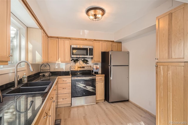 kitchen featuring dark countertops, light brown cabinets, appliances with stainless steel finishes, and a sink