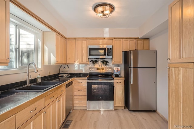 kitchen with light brown cabinets, stainless steel appliances, a sink, and tile countertops