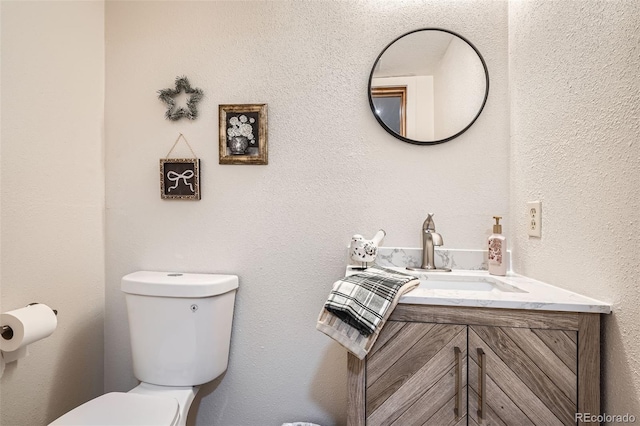 bathroom featuring toilet, a textured wall, and vanity