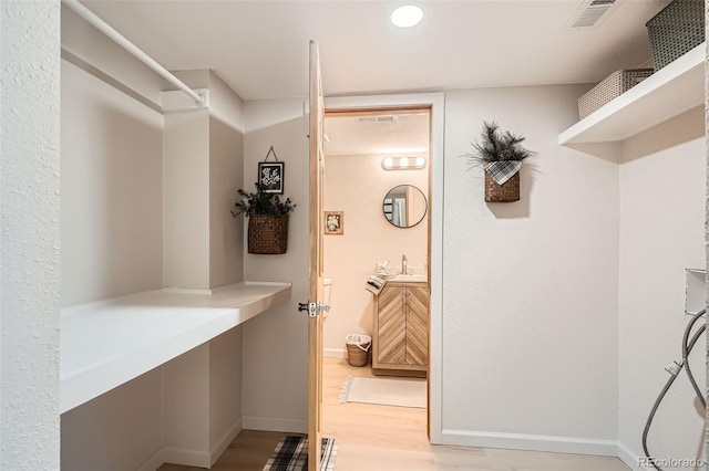 spacious closet with light wood-style floors, visible vents, and a sink