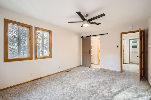 unfurnished bedroom with a barn door, light colored carpet, a ceiling fan, baseboards, and visible vents