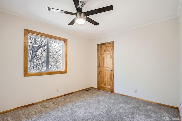 carpeted spare room featuring crown molding, a ceiling fan, visible vents, and baseboards