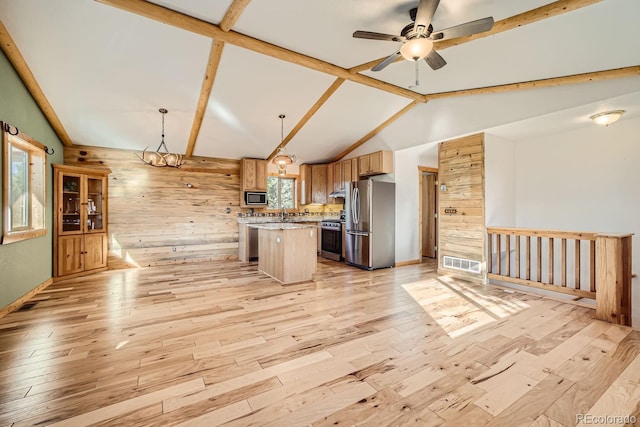 kitchen with a kitchen island, decorative light fixtures, wooden walls, appliances with stainless steel finishes, and light wood-type flooring