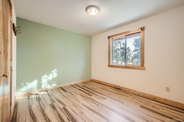 empty room with light wood-type flooring and a textured ceiling