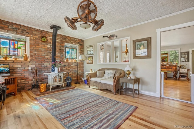 living area with brick wall, ornamental molding, light wood-type flooring, and a wood stove