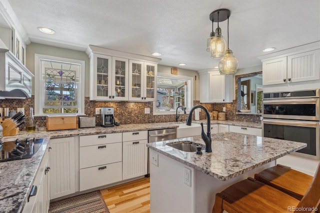 kitchen with sink, an island with sink, a kitchen breakfast bar, white cabinetry, and stainless steel appliances