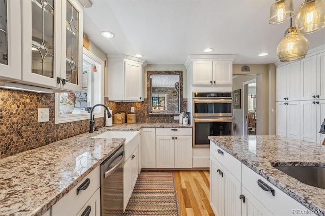 kitchen with appliances with stainless steel finishes, white cabinets, sink, and hanging light fixtures