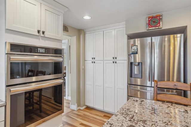 kitchen featuring light hardwood / wood-style floors, stainless steel appliances, light stone countertops, and white cabinets