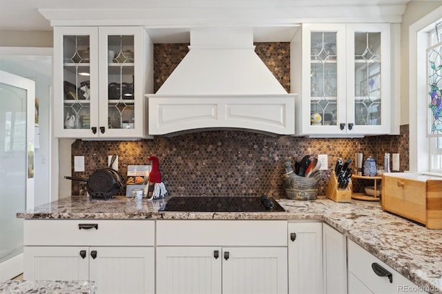 kitchen with white cabinets, backsplash, premium range hood, black electric stovetop, and light stone counters