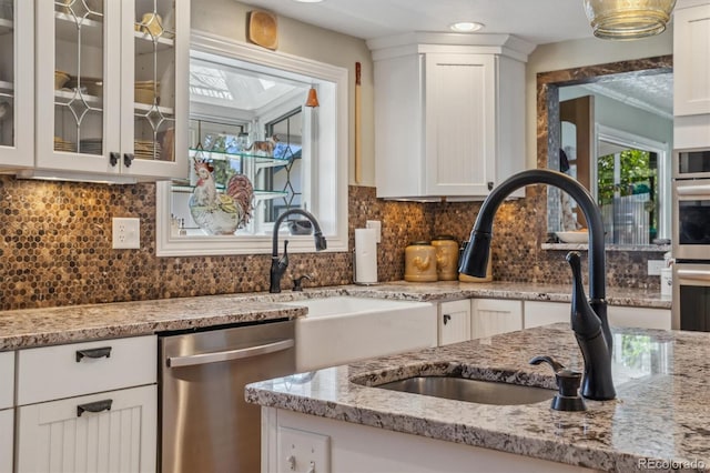 kitchen with light stone countertops, sink, dishwasher, and white cabinetry