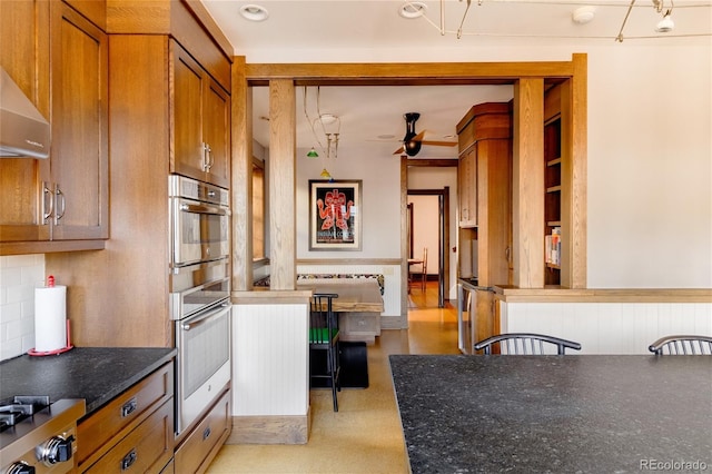 kitchen with double oven, wall chimney exhaust hood, ceiling fan, and stove