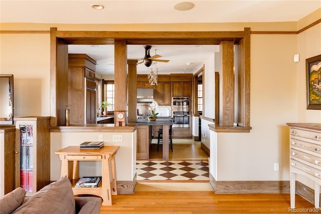 kitchen featuring hanging light fixtures, kitchen peninsula, double oven, light tile flooring, and ceiling fan