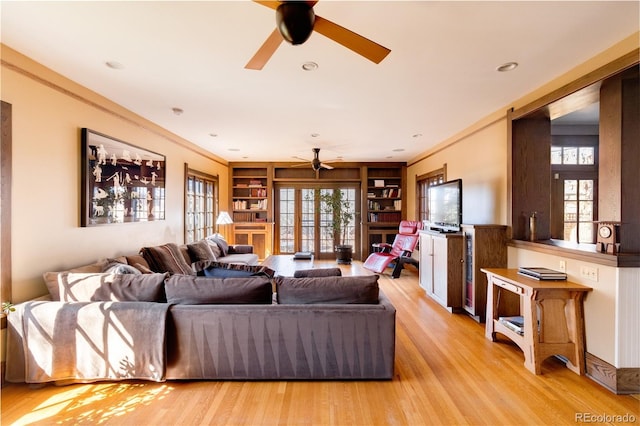 living room with built in features, ceiling fan, crown molding, light wood-type flooring, and french doors