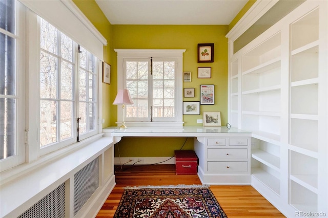 home office with radiator, built in desk, and light wood-type flooring