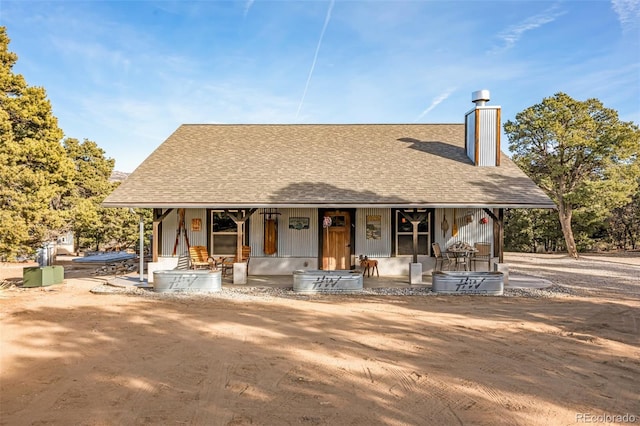 view of front facade with covered porch, a chimney, and a shingled roof