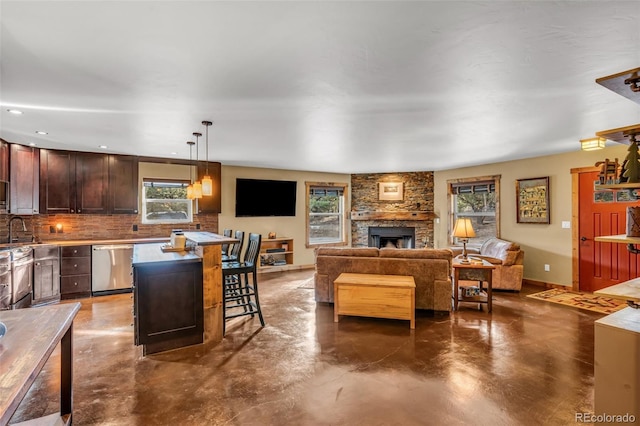 kitchen featuring finished concrete floors, a stone fireplace, a sink, stainless steel dishwasher, and backsplash