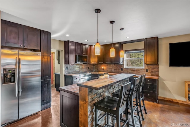 kitchen with butcher block counters, appliances with stainless steel finishes, concrete floors, hanging light fixtures, and a center island