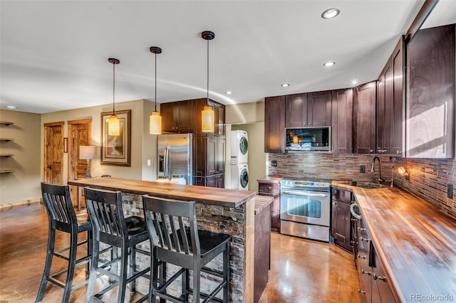 kitchen with a sink, finished concrete floors, stacked washer and clothes dryer, appliances with stainless steel finishes, and wood counters