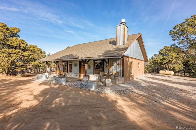 view of front of house with a patio, a chimney, and a shingled roof