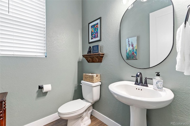 bathroom with a textured wall, toilet, baseboards, and wood finished floors