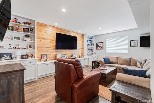 living room featuring built in shelves, light wood-type flooring, and wood walls